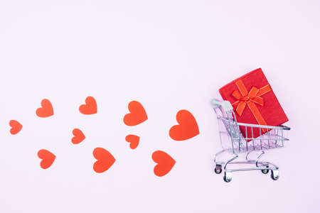 Shopping cart with red gift box. Pink Background for Valentine's day. Hearts fly from the cart with a giftの写真素材