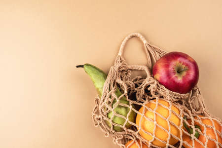 Fresh fruits and vegetables in a wicker eco-friendly bag on a beige background. Zero wasteの写真素材