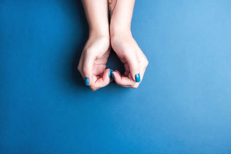 Womens hands on a blue background folded into a heart. Beautiful womens manicure, a tattoo on the handの写真素材