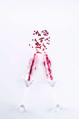 Two champagne glasses with sparkly hearts. Small red hearts scattered from the collision of glasses. Valentines dayの写真素材