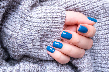 Stylish women's manicure in blue on the background of a knitted gray jacket. The concept of self-careの写真素材