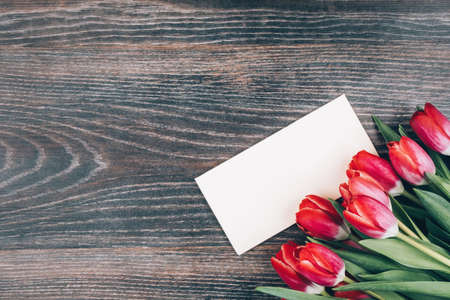 Dark wooden background with red tulips and a postcard for text. Beautiful design for a women's holiday. Bouquet of flowers for mom. Space for textの写真素材