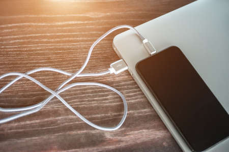 The phone is charged from a laptop. modern gadgets on the table.の写真素材