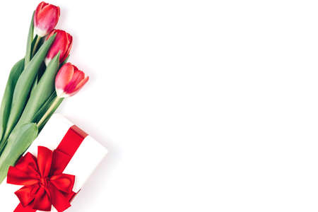 Red Tulips and a gift box with a large bow on a white background. Beautiful background for international women's day. Place for text, isolateの写真素材