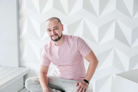 A young man in a pink t-shirt with a beard is smiling. Beautiful athletic male figure. The concept...