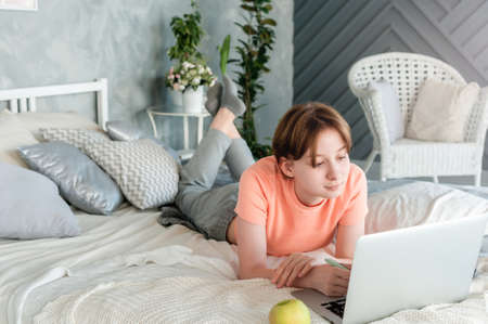 A teenage girl at home is lying on a bed with a laptop in headphonesの写真素材