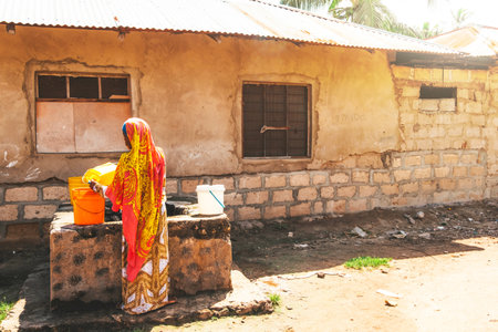 Pwani Beach, Zanzibar, Tanzania. 26 November 2020: girl in bright clothes draws water from a well. Village life on the island of Zanzibar. Beautiful national womens clothing. Life styleのeditorial素材