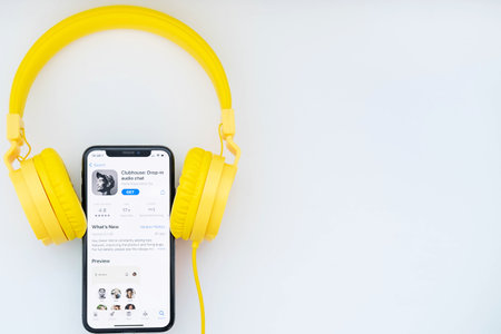 February 16, 2021, Russia, Orenburg: iPhone and yellow headphones on a white background. Clubhouse application on the phone screen. New social network powered by Apple.のeditorial素材