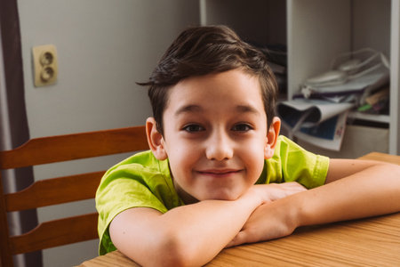 Smiling young boy leaning on folded arms at table concept of childhood happiness and relaxation for design, card, poster, background.の写真素材