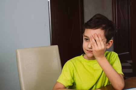 Young boy covering one eye at table concept of childhood boredom and emotion for design, card,...