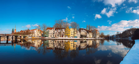 Old Town riverfront with colorful historic houses reflected in calm Trave River under blue sky and...
