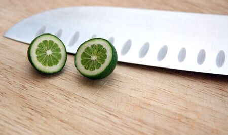 Tiny baby lime on cutting board with chef's knife.  Strange perspective with tiny lime and large knife.の写真素材