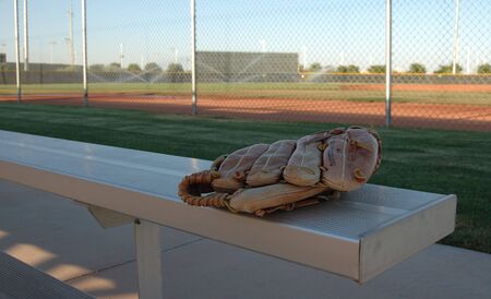 Image of a baseball glove on a fan bleacher.  The ball field is seen being watered in the background .の写真素材