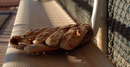 The soft glow of sunset falls on a baseball glove left on the bench after the game.の写真素材