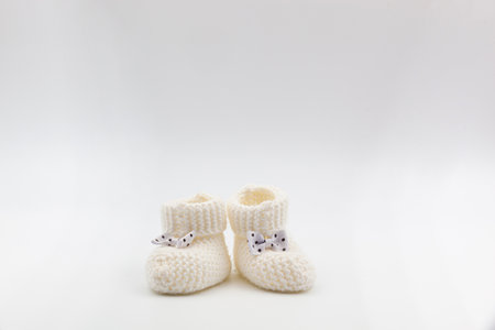 White knitted baby booties with bows on a gray isolated background