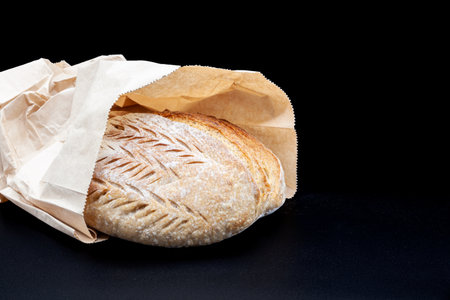 Freshly baked Vermont rye bread with crisp crust and porous texture in flour and bemag bag on black...