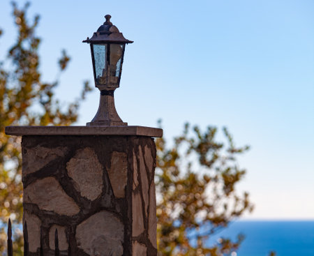 Small lamp lamp on a stone pillar. In the background a tree and blue sea. High quality photo.の写真素材