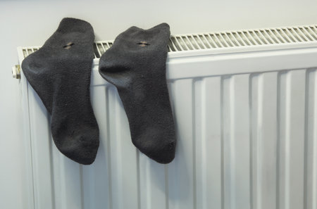 An everyday scene with dark socks hanging on a modern radiator. The concept of home comfort, energy saving, drying laundry, and the start of the heating season in the interior.の写真素材