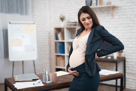 Young pregnant woman is experiencing labor in office. Pregnant in office. Pregnant belly. Pregnancy. Pregnant in office.の写真素材