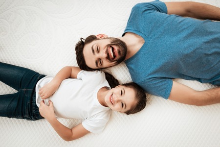 Top view of father and daughter. Adult happy bearded man with cute little daughter lies on bed in mattress store. Testing softness of mattress. Check softness of mattress.の写真素材