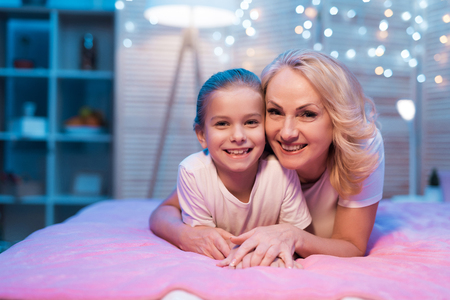 Grandmother and granddaughter are hugging on bed at night at home. Grandma and child on bad.の写真素材