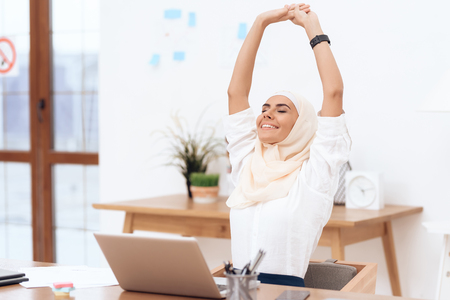 The arab woman in the hijab relaxes. She is sitting at the desk in the office. She has a little break.の写真素材