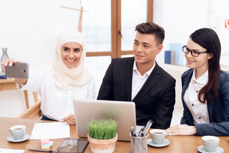 A woman in hijab makes selfie with her colleagues. They are engaged in business.の写真素材