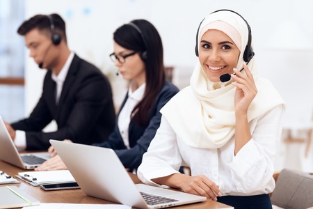 An Arab woman works in a call center. She's an operator. Her colleagues work nearby.の写真素材