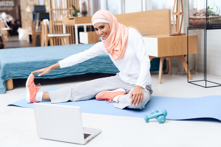 Arab woman doing gymnastics in the bedroom. She's at home. She has a headscarf on her head.の写真素材
