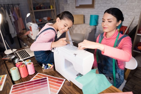 Mom and daughter are working together on the creation of clothes. They are in the sewing workshop in the evening.の写真素材
