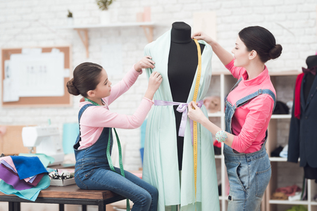 A little girl gives a woman a pin. They are with mom in the sewing workshop. Mom sews on the sewing machine.の写真素材