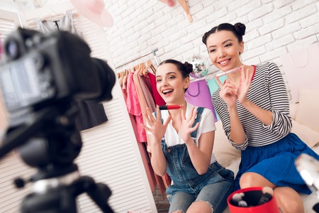 Two fashion blogger girls in jeans and shirt with skirt hold up colorful lipstick to camera.の写真素材