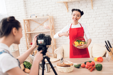 Two culinary bloggers in red aprons mixing diced peppers with salad to camera.の写真素材