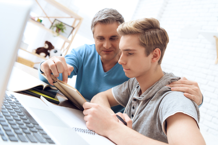 Father helps his son who is doing homework. Troubled teenager tries to study. Father embraces his son.の写真素材