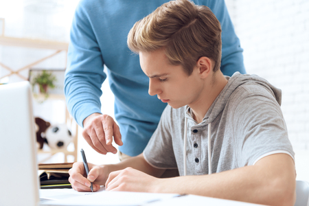 Father helps his son do homework. Father shows troubled teenager right answer. Points his finger.の写真素材