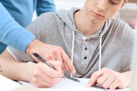 Father helps his son do homework. Father shows troubled teenager right answer. Points his finger.の写真素材