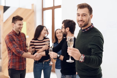 A group of young office workers celebrating. They hold glasses with alcohol in their hands. They are in a good mood.の写真素材