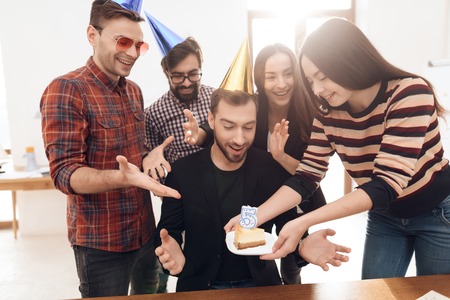 The office staff surprises their manager. They celebrate the anniversary of the company. They are dressed in holiday caps.の写真素材