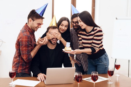 The office staff surprises their manager. They celebrate the anniversary of the company. They are dressed in holiday caps.の写真素材