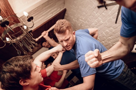 Red team hooligan fans and blue team hooligan fans are fighting at sports bar. They are watching football game.の写真素材