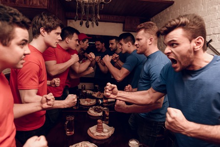 Red team fans and blue team fans are fighting at sports bar. They are watching football game.