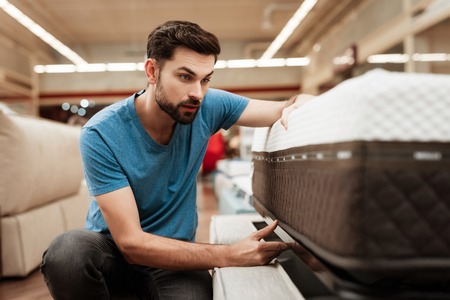 Handsome bearded man is testing mattress in furniture store. Orthopedic mattress for a healthy posture. Checking mattress in furniture store.の写真素材