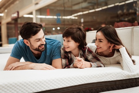 Lovely bearded man, together with his beautiful wife and son, relaxes on the mattress in the store. Choosing mattress in store.の写真素材