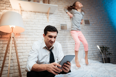 Businessman working on tablet. Little girl prevents her father from working. Schoolgirl has fun next to his father. Busy fatherの写真素材