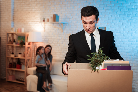 Adult man leaves house with stuff box. Father leaves home because of problems in family. Family problems. Businessman is carrying box.の写真素材