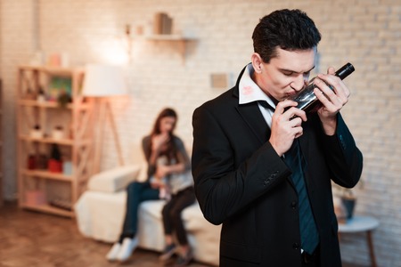 Adult man in suit drinks alcohol at home. Family alcoholic kiss bottle. Mother and daughter are alarmed by alcoholism of drunk father.の写真素材