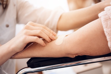 Close up. Girl is nursing elderly woman in wheelchair at home. Girl is using drop counter to help woman.の写真素材