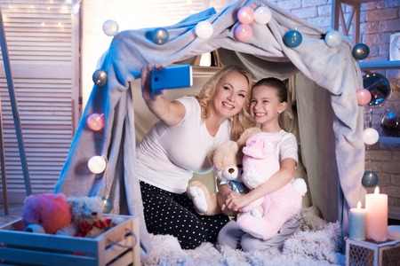Grandmother and granddaughter are taking selfie in cozy blanket house at night at home.の写真素材