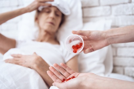 Close up. Girl is nursing elderly woman in bed at home. Red pills in cup for woman.の写真素材