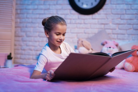 Little girl, granddaughter is reading book on bed at night at home.の写真素材